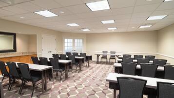 A conference room with multiple tables and chairs, carpeted floor, and a projector screen on the wall.