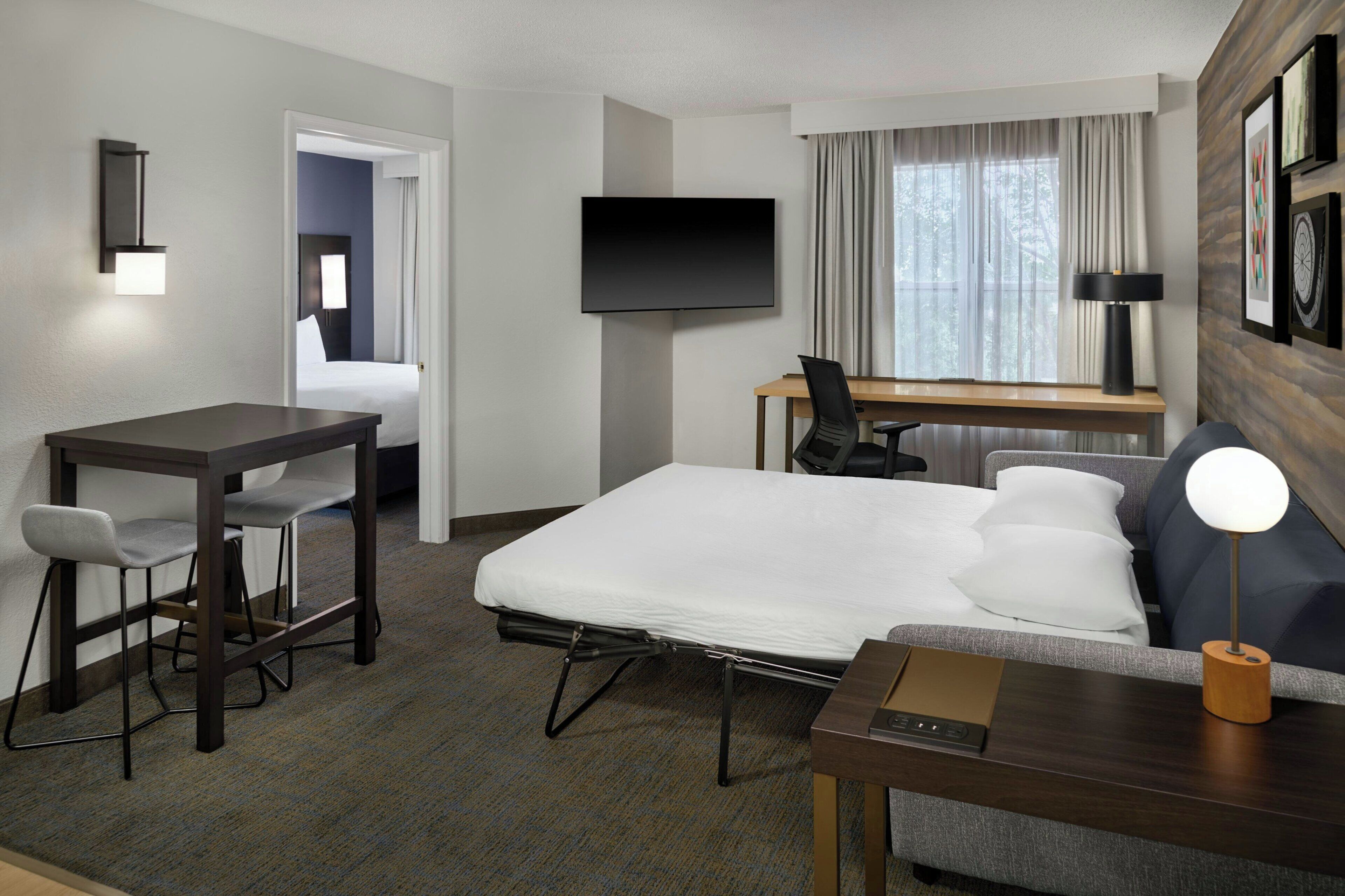 Una habitación de hotel con cama, escritorio, silla, televisor y lámpara.
