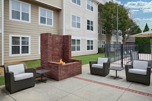 A patio with a brick fire pit, wicker furniture, and a building in the background. - Residence Inn by Marriott Huntsville (Huntsville)