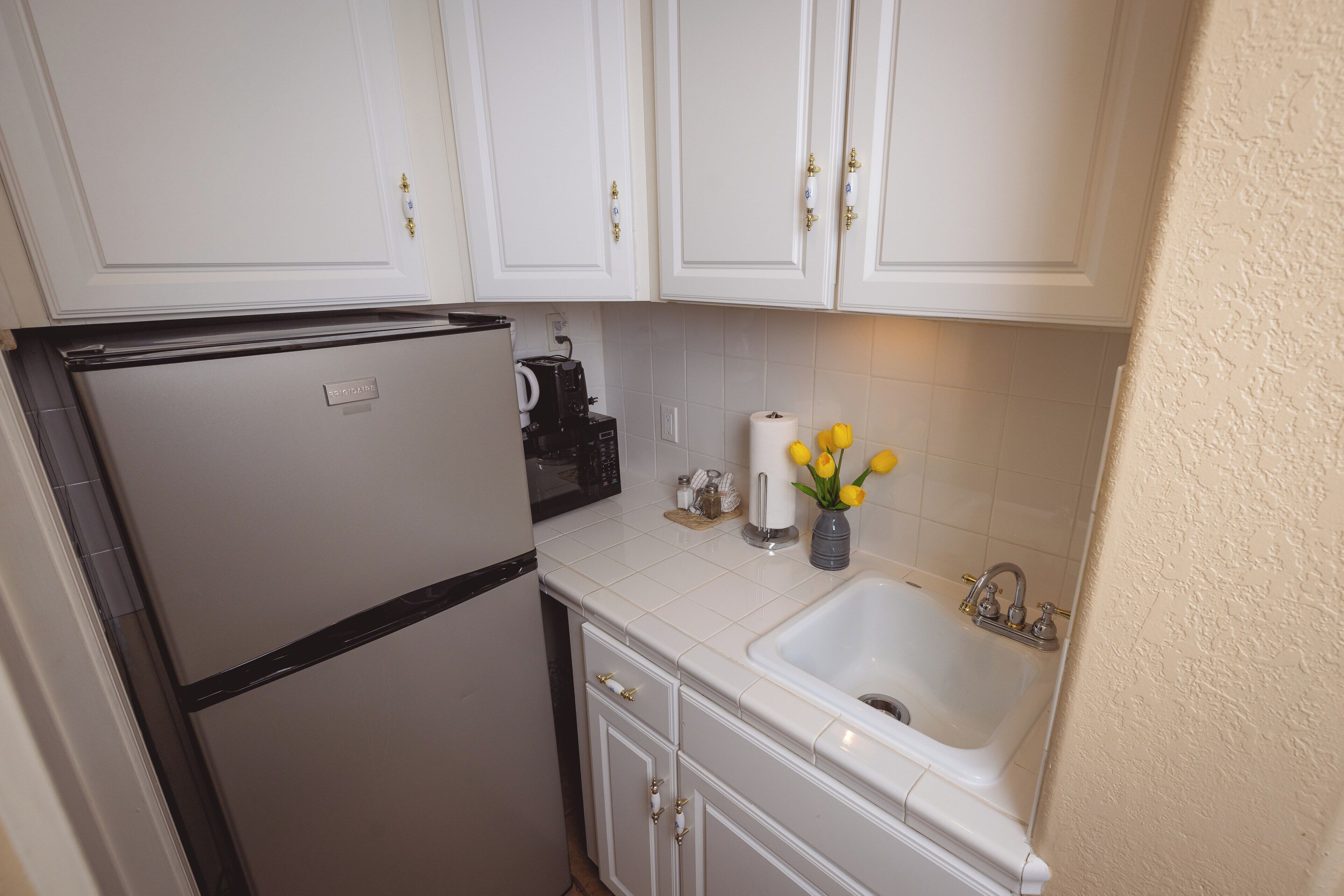 A compact kitchen with white cabinets, a built-in refrigerator, a sink, and a coffee maker.