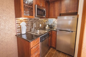 A kitchen with a stainless steel refrigerator, a microwave, a sink, and wooden cabinets.