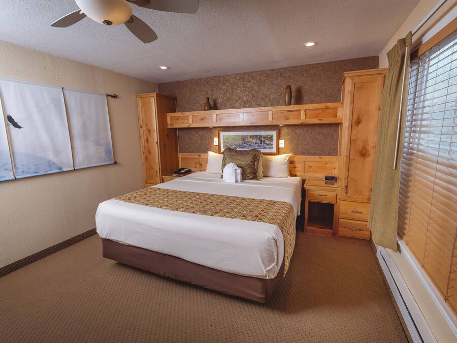 A hotel room with a large bed, a desk, a chair, a wardrobe, and a window with blinds.