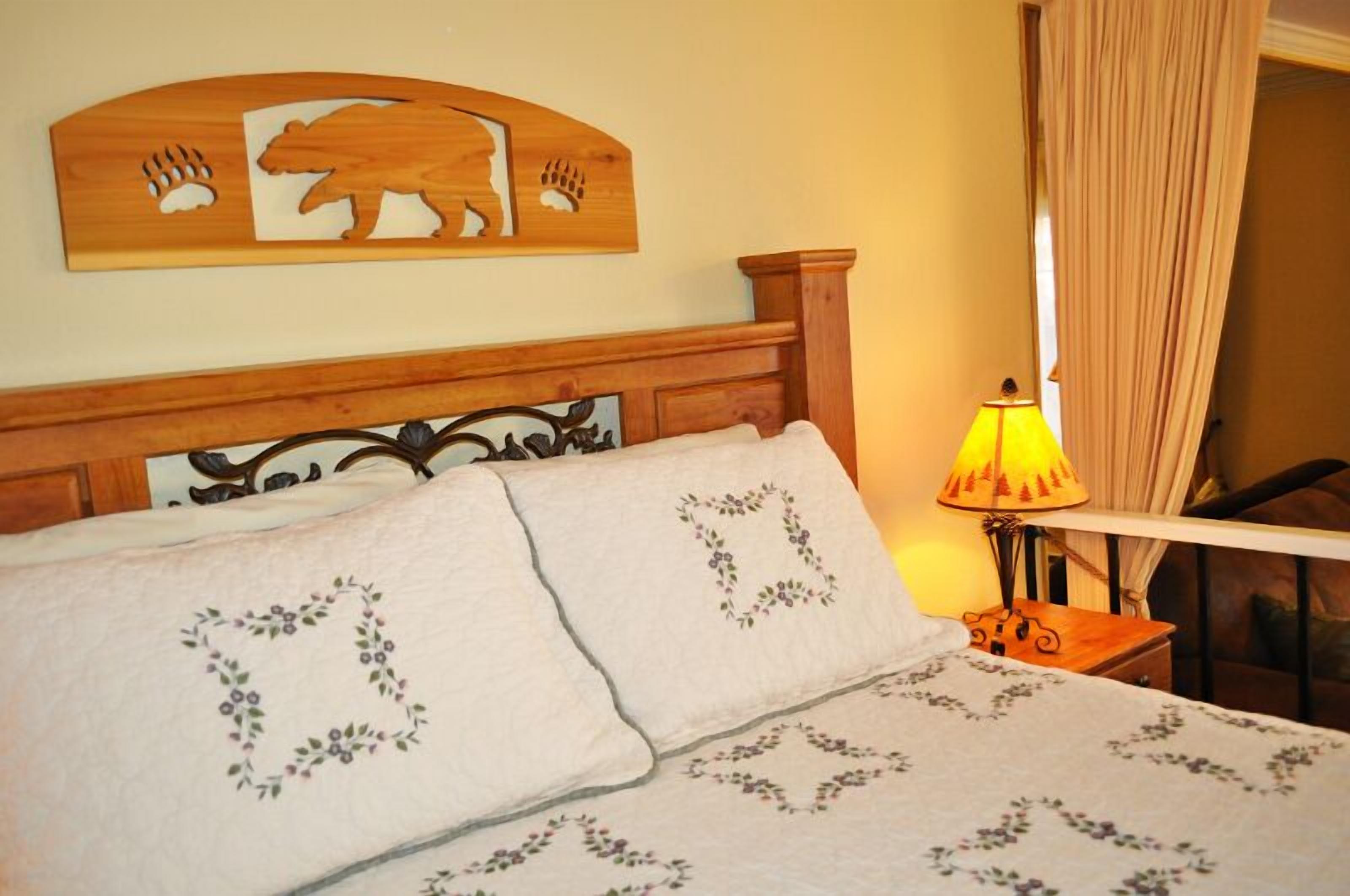 Un lit avec une literie à motifs floraux, une tête de lit en bois ornée d’un motif d’ours et une lampe de chevet.