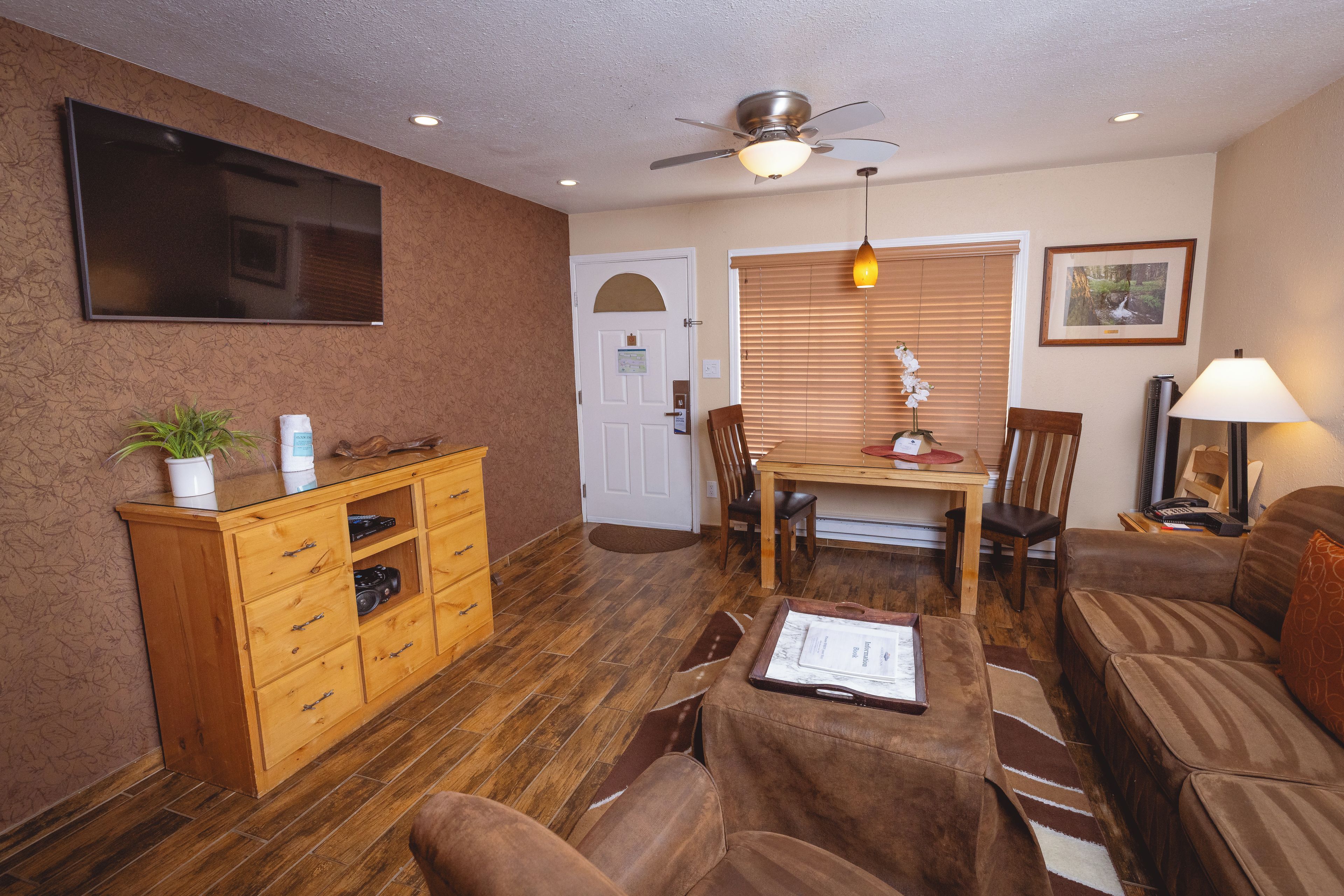 A living room with a wooden cabinet, a ceiling fan, a television, a dining table with chairs, and a sofa.