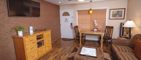 A living room with a wooden cabinet, a ceiling fan, a television, a dining table with chairs, and a sofa.