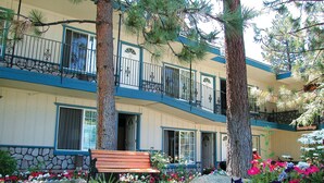 Un edificio de varios pisos con fachada de piedra, balcones con barandillas metálicas y un jardín con flores y un banco.