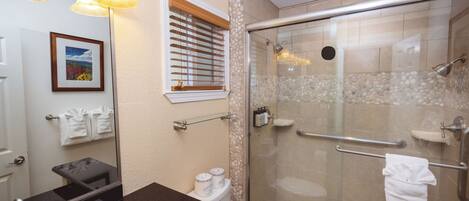 A bathroom with a glass-enclosed shower, a black countertop, a mirror, and a framed picture on the wall.