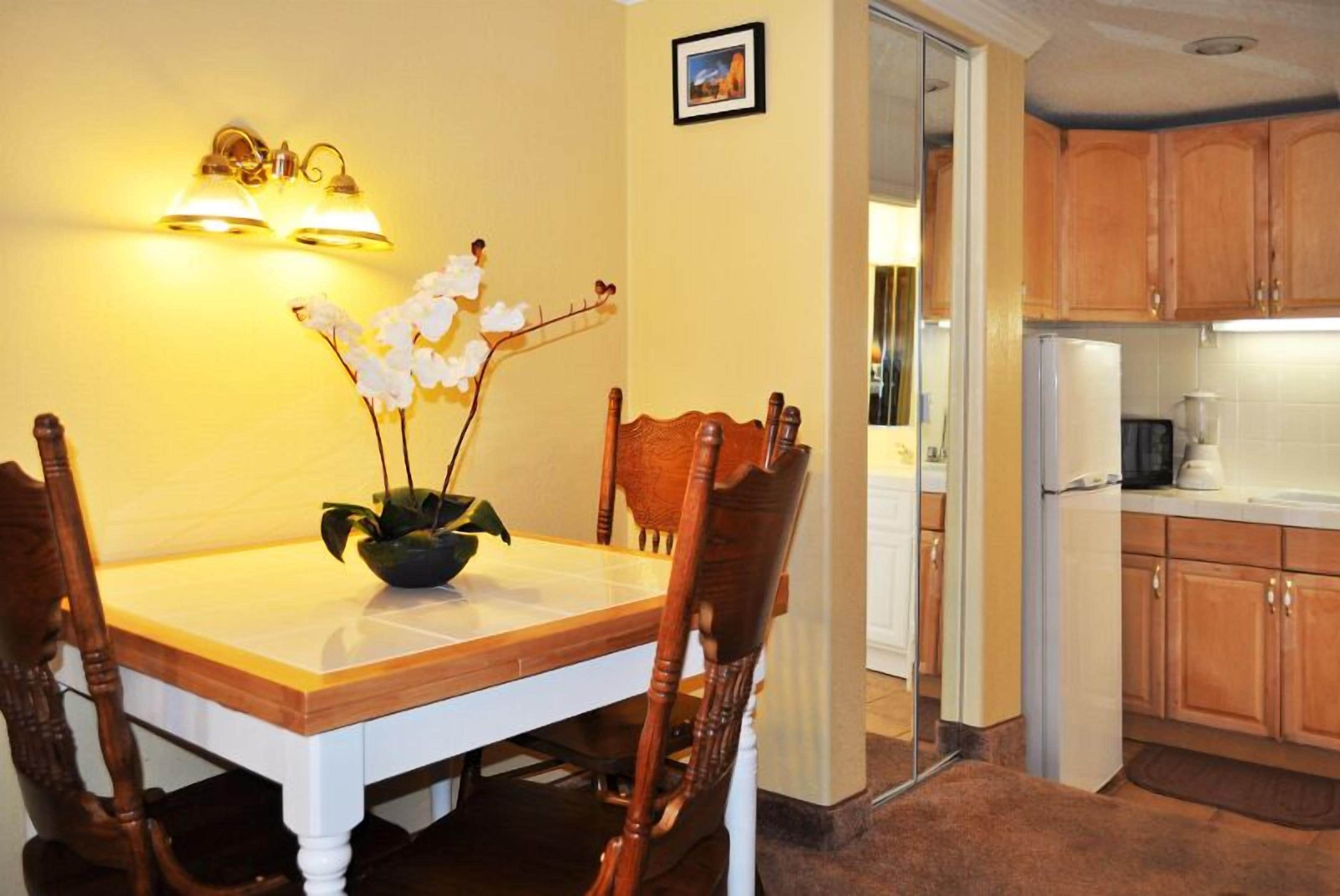 A dining area with a wooden table and chairs, a vase with flowers, and a wall-mounted light fixture.