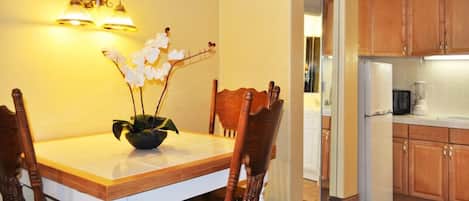 A dining area with a wooden table and chairs, a vase with flowers, and a wall-mounted light fixture.