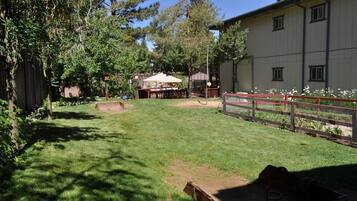 Un jardín bien cuidado con césped, cerca de madera, una mesa de picnic y un espacio cubierto.
