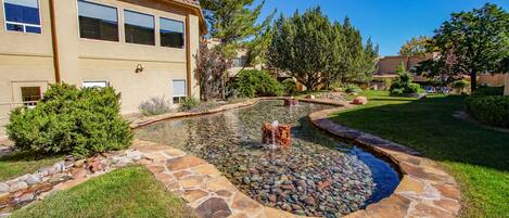 A landscaped garden with a pond, stone border, and surrounding greenery.
