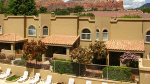 Un hotel con varias habitaciones, una zona de piscina con tumbonas y vistas a formaciones rocosas rojas.