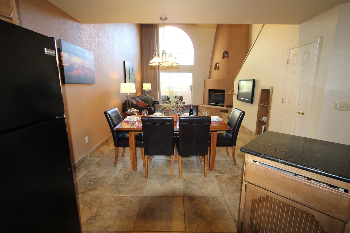 A dining area with a wooden table and chairs, a black refrigerator, and a fireplace.