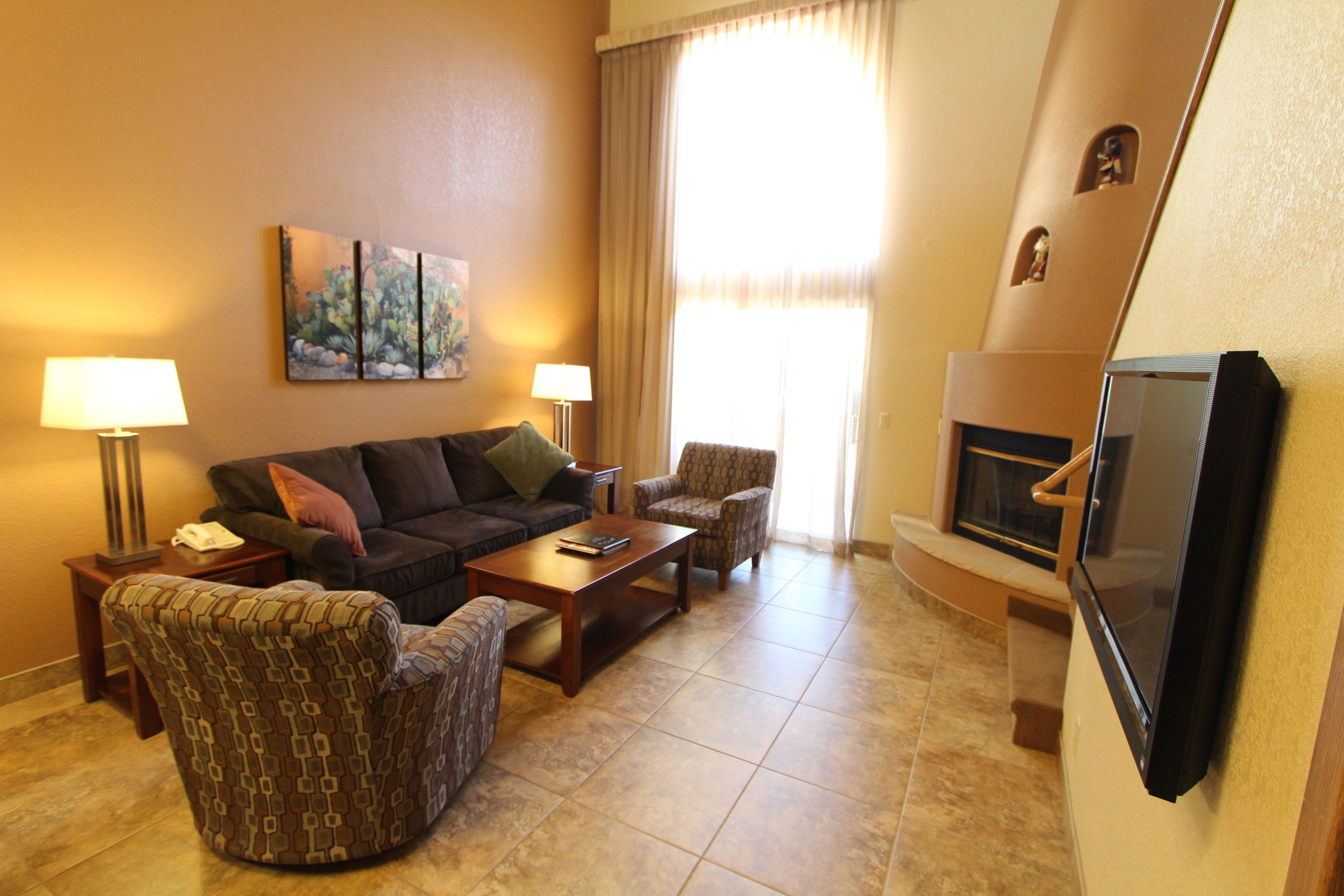 A living room with a sofa, armchairs, a coffee table, a flat-screen TV, and a fireplace.