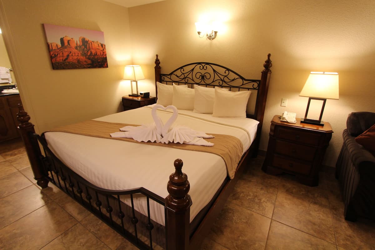 A neatly made bed with white linens, two bedside tables with lamps, and a painting on the wall.