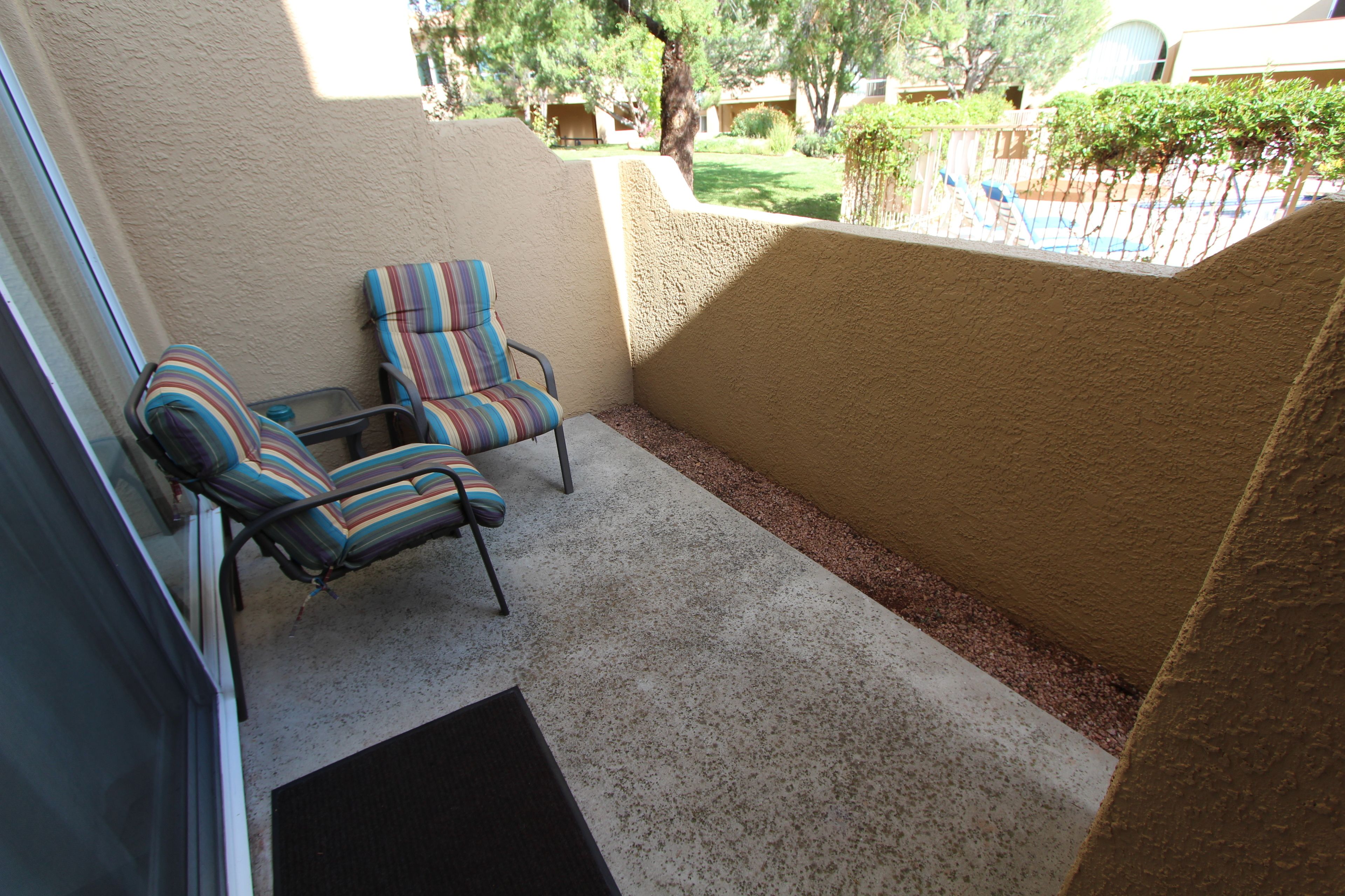 A covered patio area with two striped chairs and a small table.