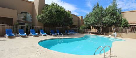 Una piscina con sillas reclinables azules y un cielo despejado.