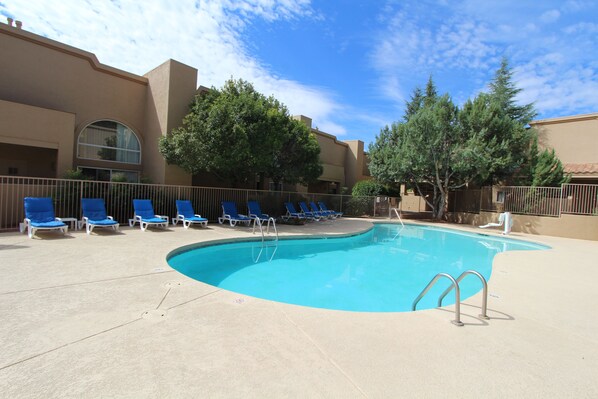 A swimming pool with blue lounge chairs and a clear sky.