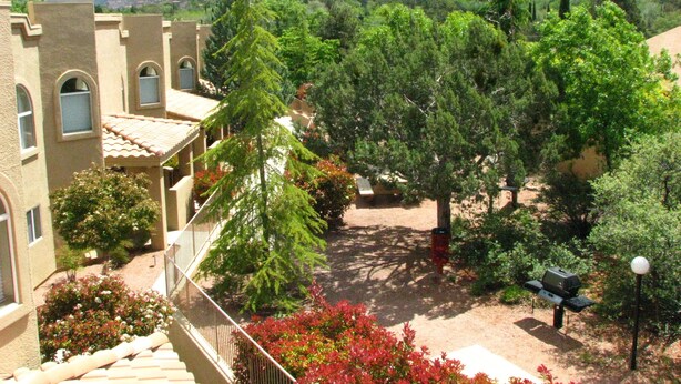Un patio con un edificio de ventanas arqueadas y techo de tejas, rodeado de exuberante vegetación y montañas al fondo.