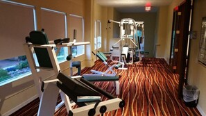 Une salle de sport d’hôtel équipée de matériel d’exercice, dotée de grandes fenêtres et recouverte d’un tapis à motifs.