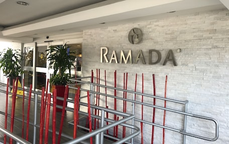 Una entrada moderna con un letrero que dice "RAMADA" y una escalera con barandales rojos y plateados.