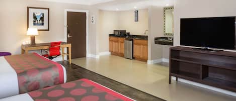 Une chambre d’hôtel avec deux lits, un bureau avec une chaise, une télévision, un coin cuisine et une salle de bain.