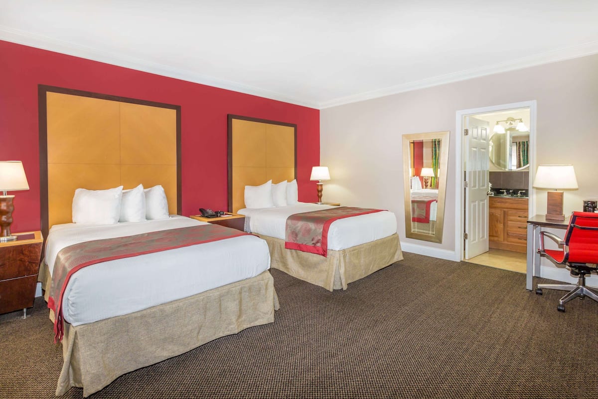 A hotel room with two beds, a desk, and a chair.