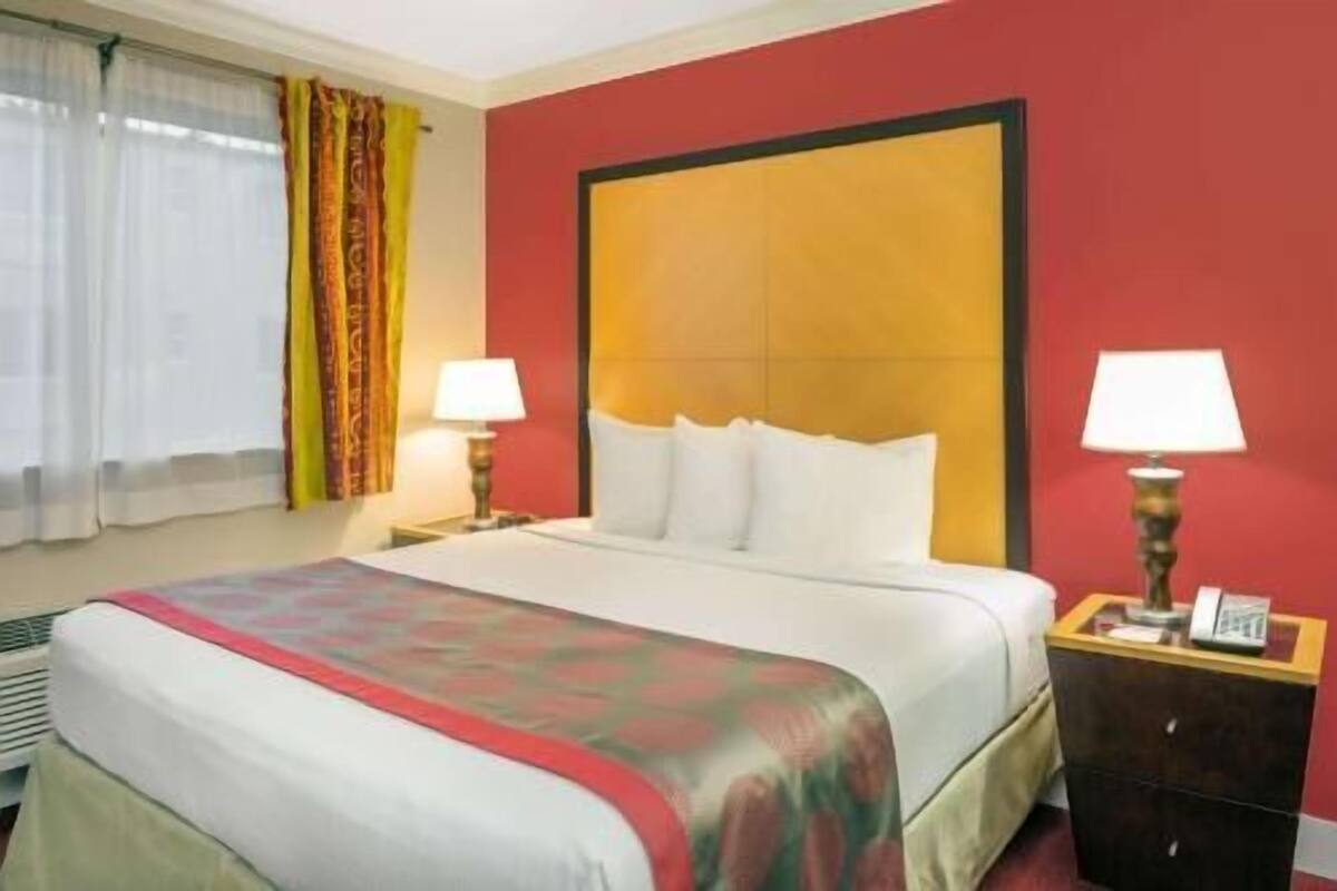 A hotel room with a bed, two bedside tables with lamps, a window with curtains, and a red accent wall.