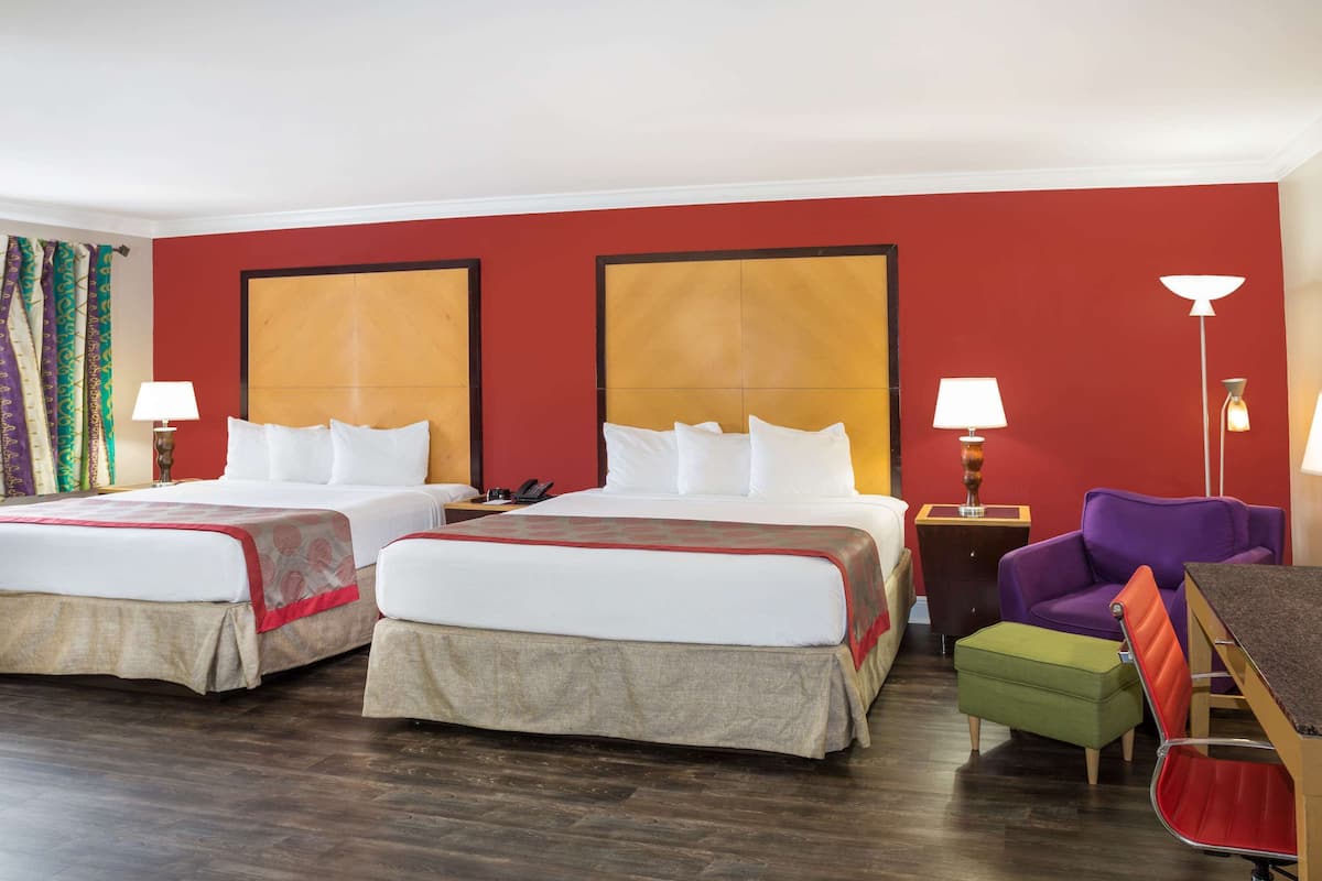 A hotel room with two beds, a desk, a chair, a small table, and a lamp.