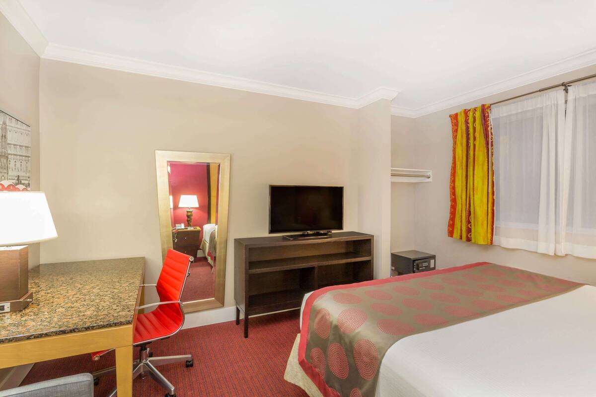 A hotel room with a bed, a desk with a chair, a television, and a mirror.