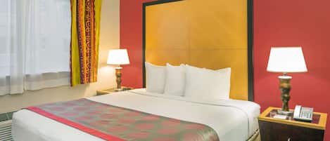 Una camera d'albergo con un letto grande, due comodini con lampade, una parete di colore rosso e una finestra con tende.