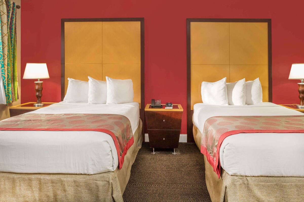 A hotel room with two beds, each with a wooden headboard, a nightstand, a lamp, and a small dresser.