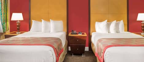 A hotel room with two beds, each with a wooden headboard, a nightstand, a lamp, and a small dresser.