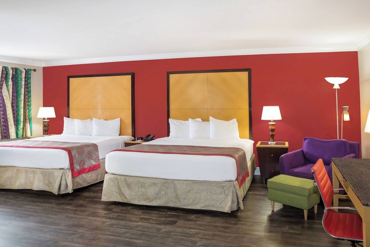 Habitación de hotel con dos camas, un escritorio, una silla morada y un reposapiés verde.
