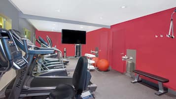A gym with treadmills, a bench, exercise balls, and a TV on the wall.