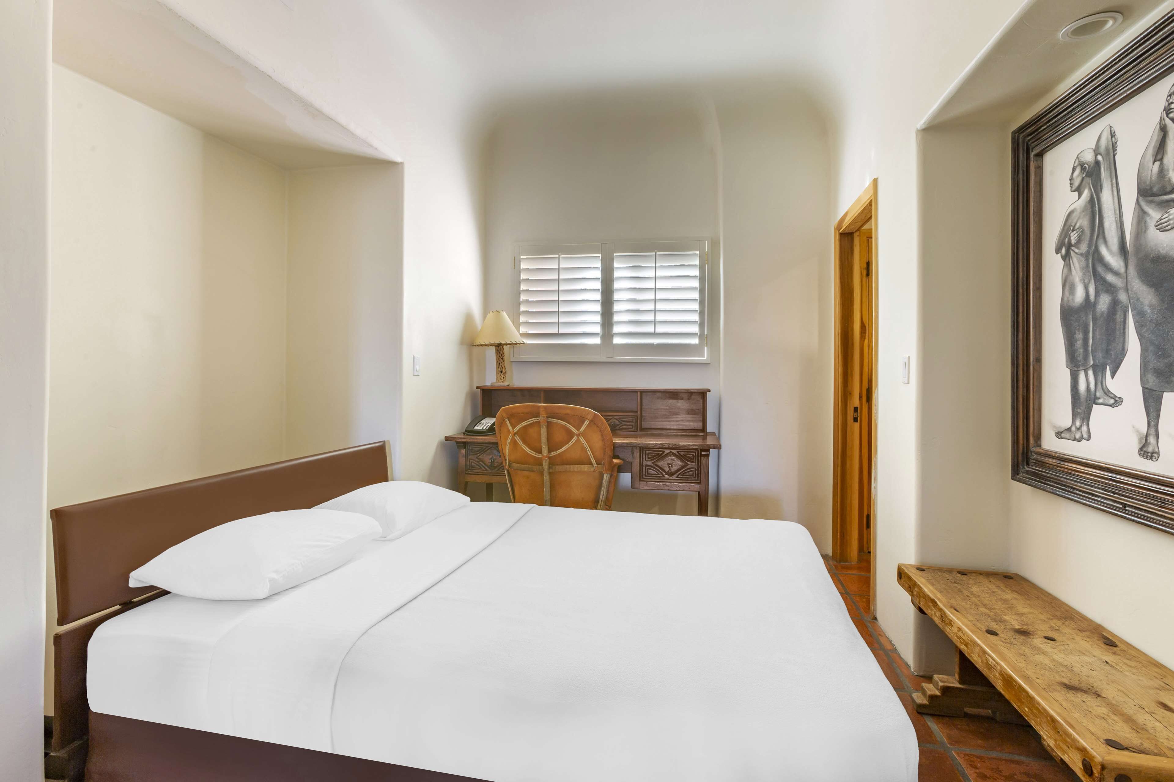 Una camera da letto con un letto, una scrivania, una sedia, una finestra con tende e un quadro appeso al muro.