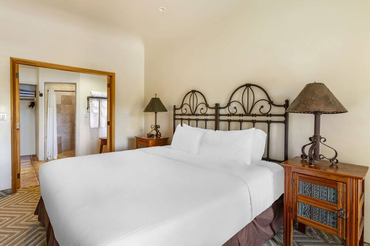 A neatly made bed with a wooden headboard, a bedside table with a lamp, and a mirror on the wall.