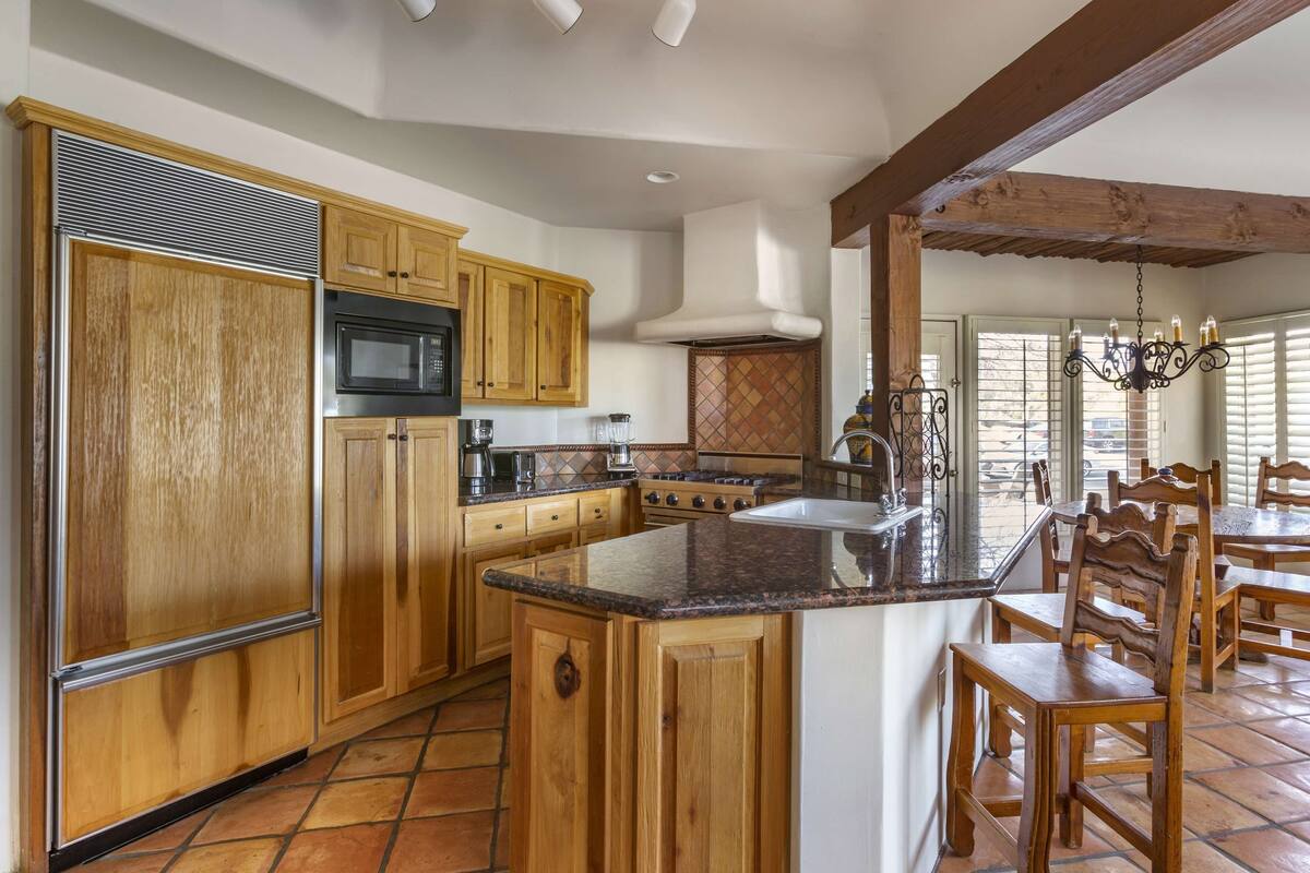 A kitchen with wooden cabinets, a central island, and a dining area with wooden chairs.