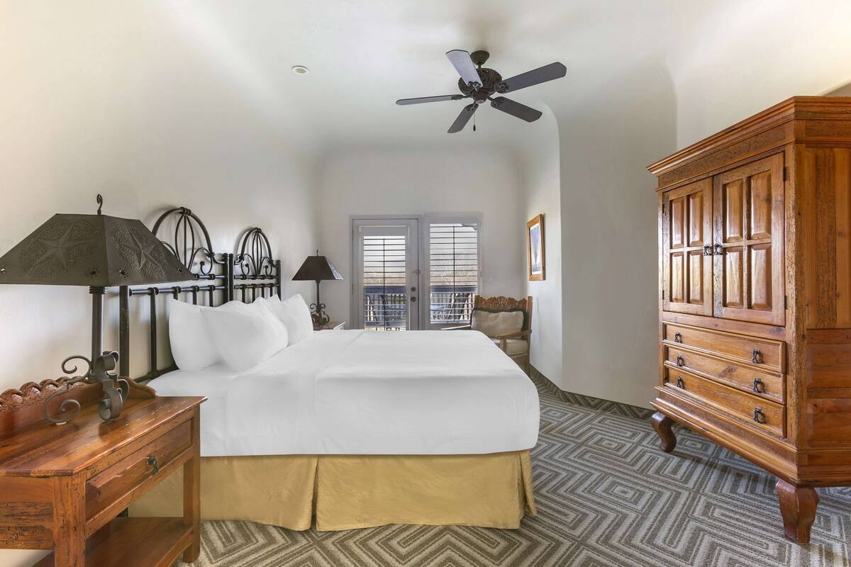 A hotel room with a bed, wooden dresser, ceiling fan, and patterned floor.