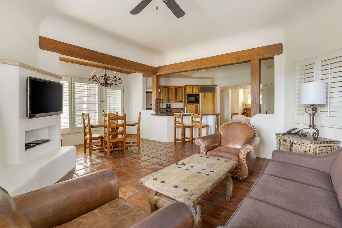 A spacious living room with a fireplace, a dining area with wooden furniture, and a kitchen visible through an open doorway.
