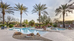 A pool area with lounge chairs, palm trees, and a clear sky.