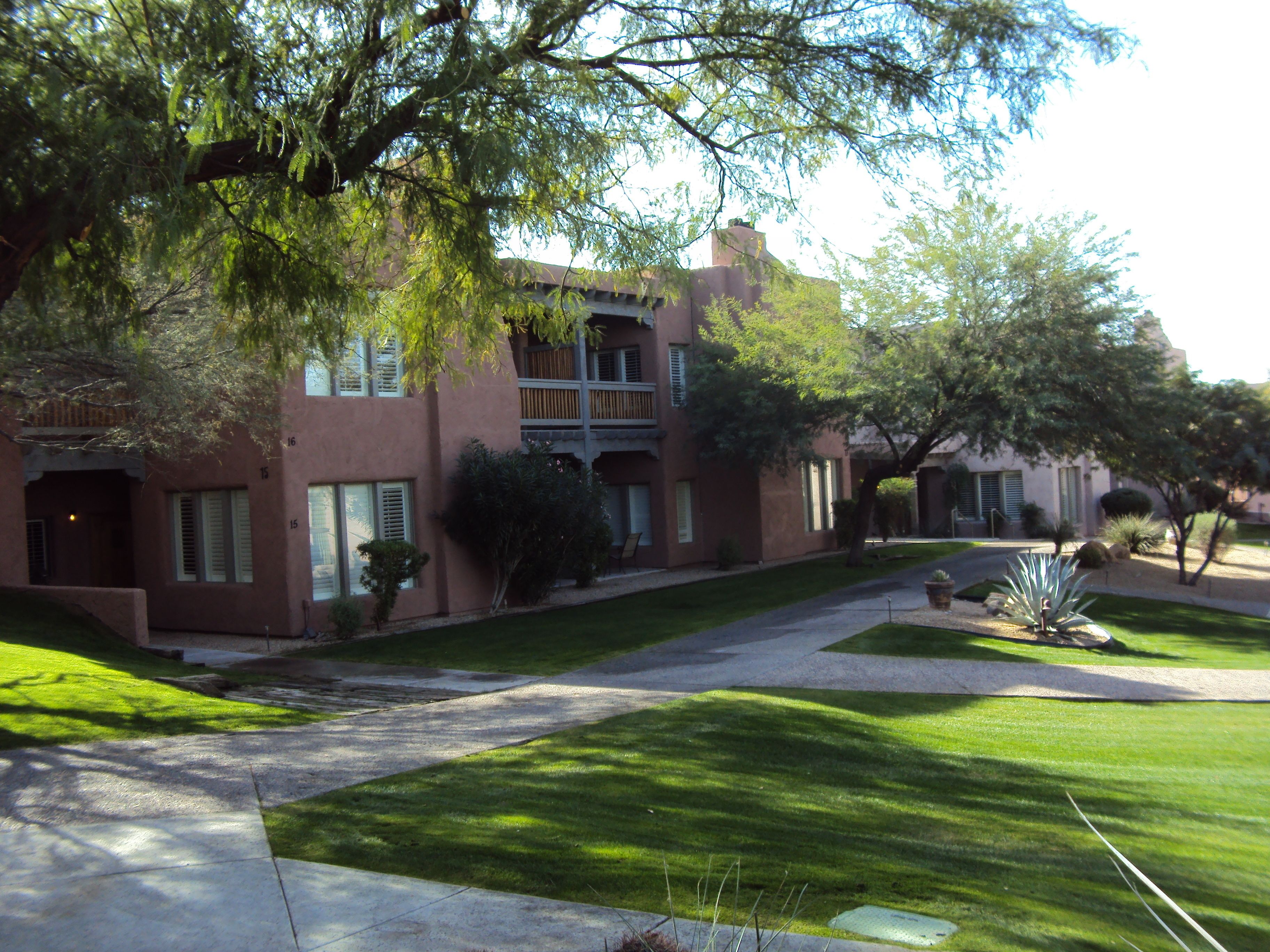 A multi-story building with a courtyard, featuring a mix of brick and stucco exteriors, a central lawn, and surrounding trees.