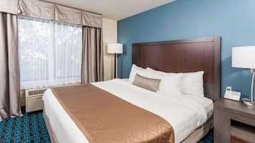 Habitación de hotel con una cama grande, una mesita de noche con lámpara y una ventana con cortinas.