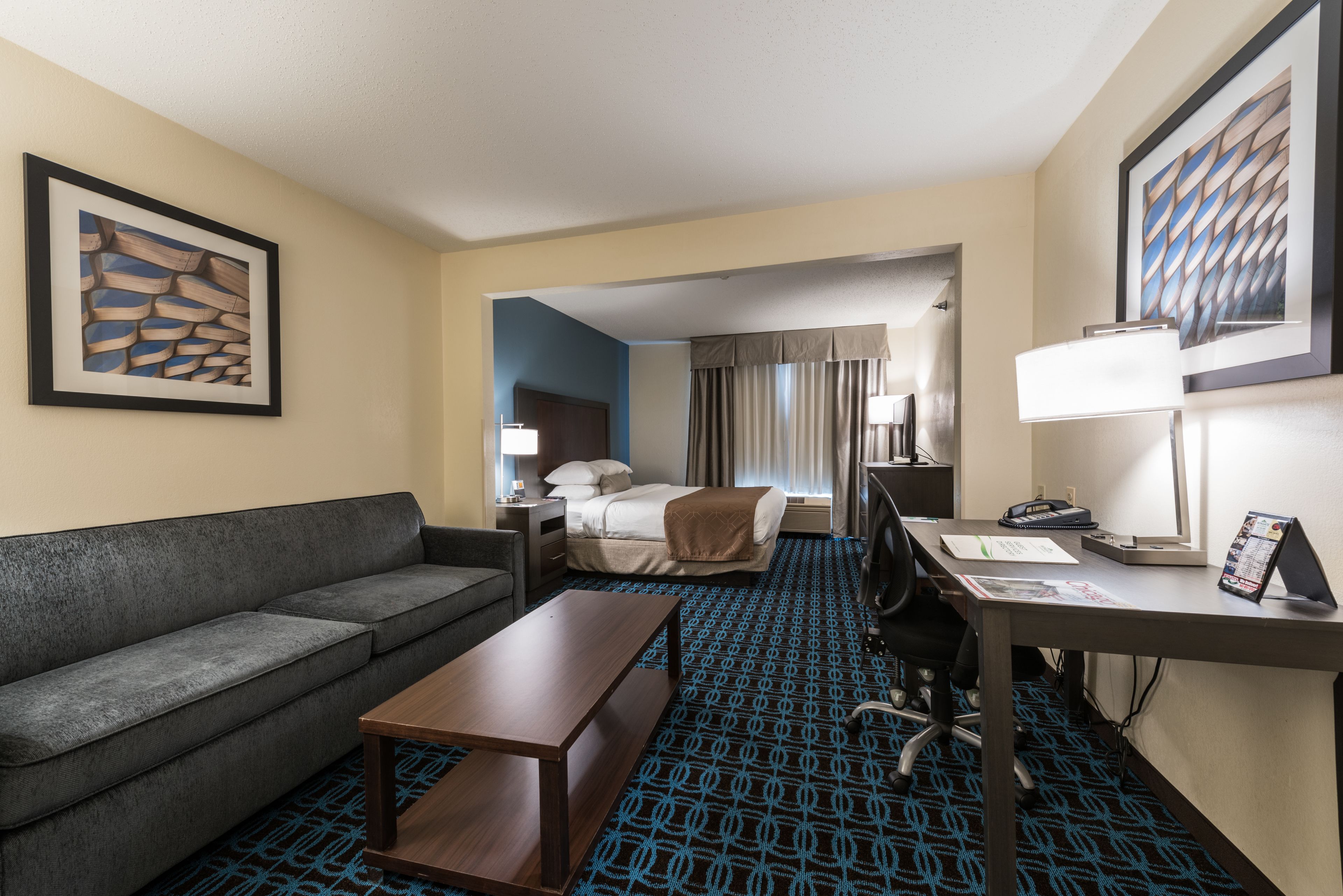 A hotel room with a sofa, a desk, a bed, a lamp, and a framed picture on the wall.