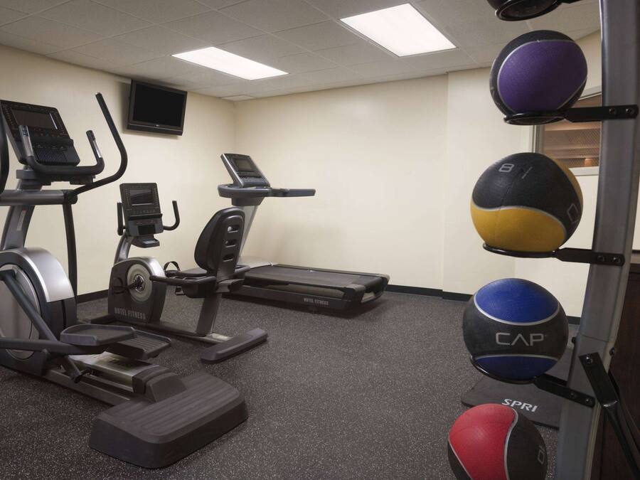 Ein Fitnessraum mit Laufbändern, einem stationären Fahrrad und einem an der Wand befestigten Medizinballhalter.
