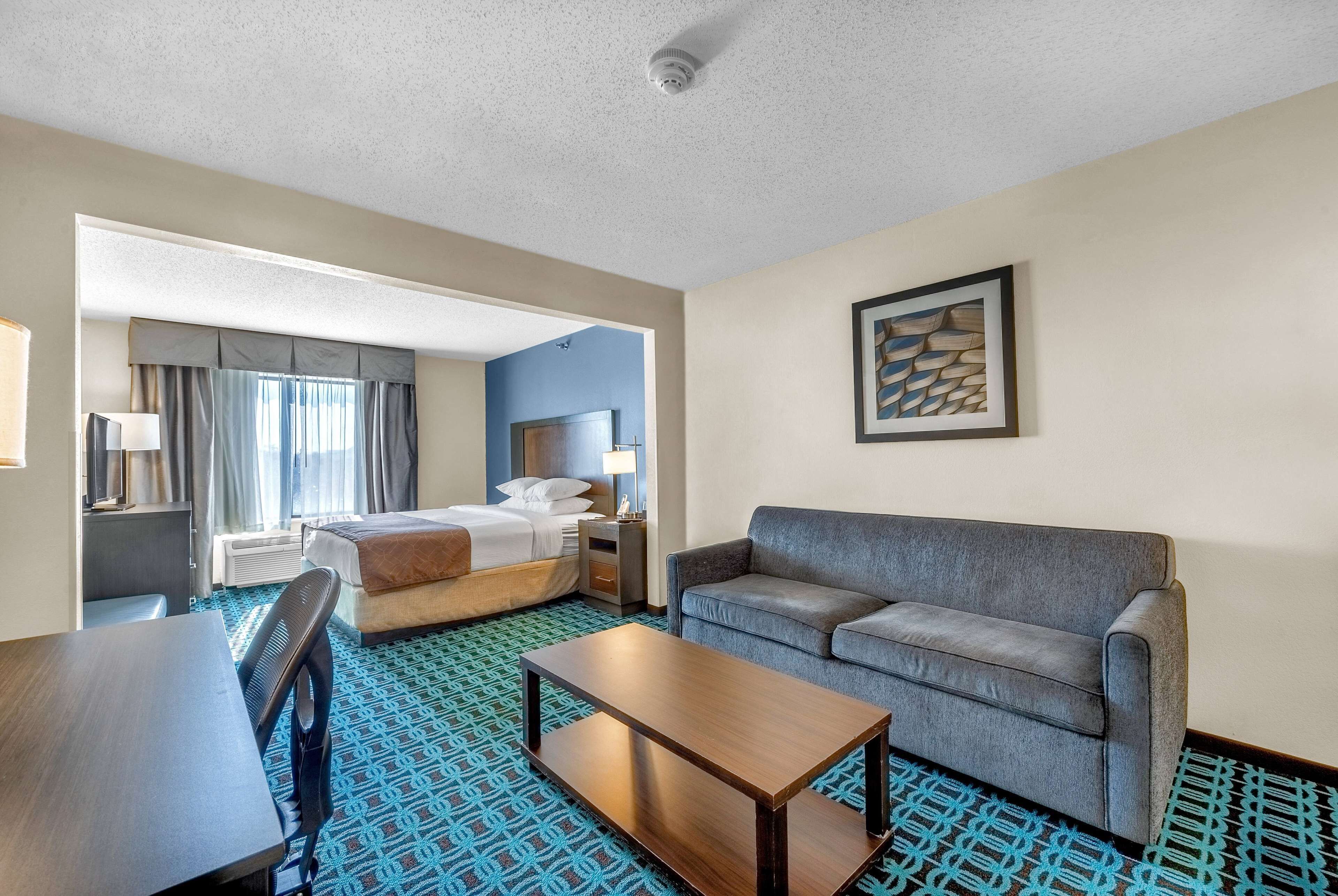A hotel room with a bed, a sofa, a desk, and a patterned carpet.