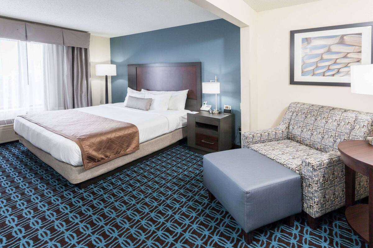 A hotel room with a large bed, a sofa, a small table, and a patterned carpet.