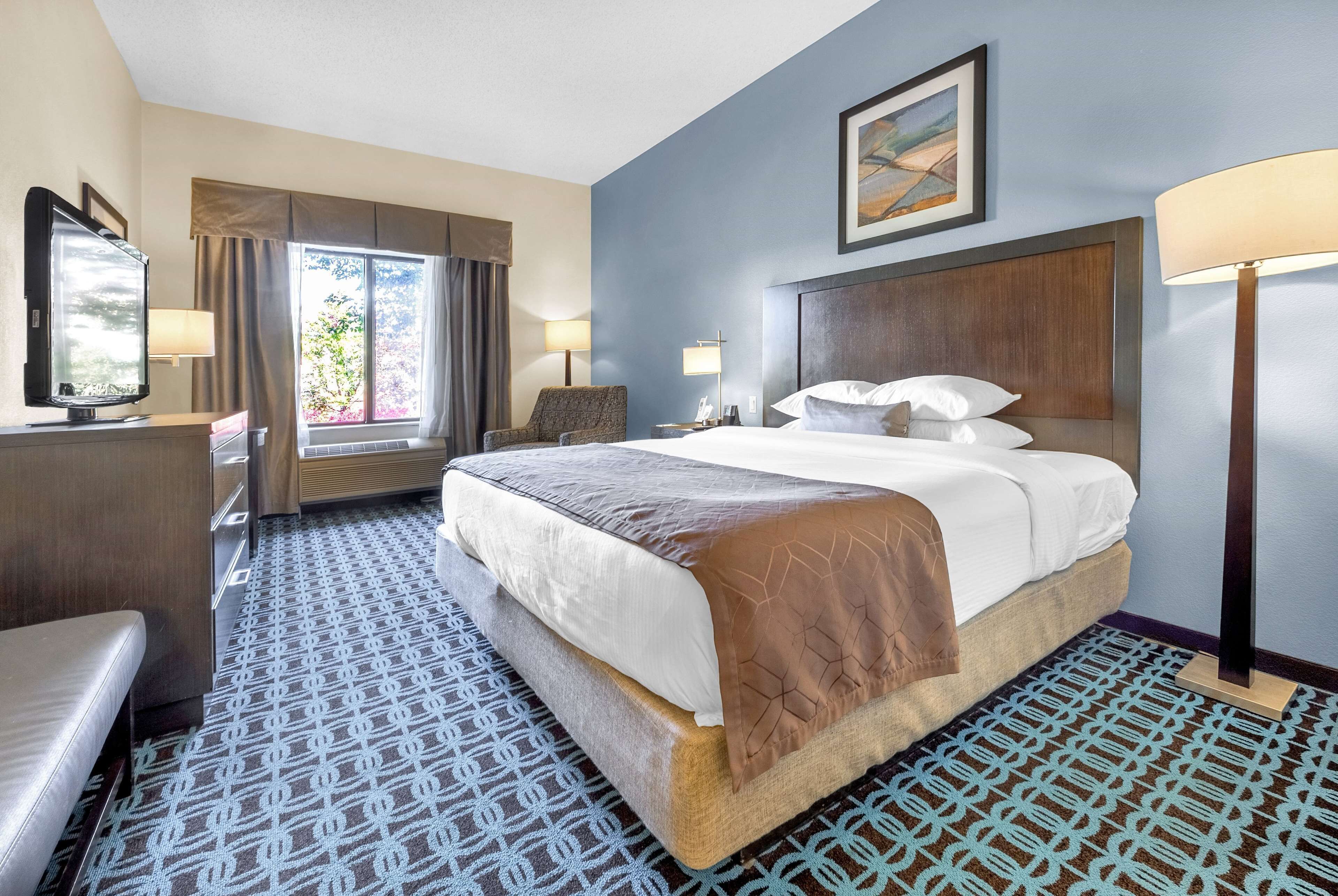 A hotel room with a large bed, two bedside lamps, a chair, a desk, and a window with curtains.