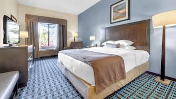 A hotel room with a large bed, two bedside lamps, a chair, a desk, and a window with curtains.