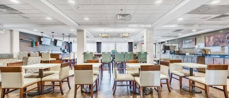A spacious dining area with multiple tables and chairs, a kitchen in the background, and a clean, modern design.